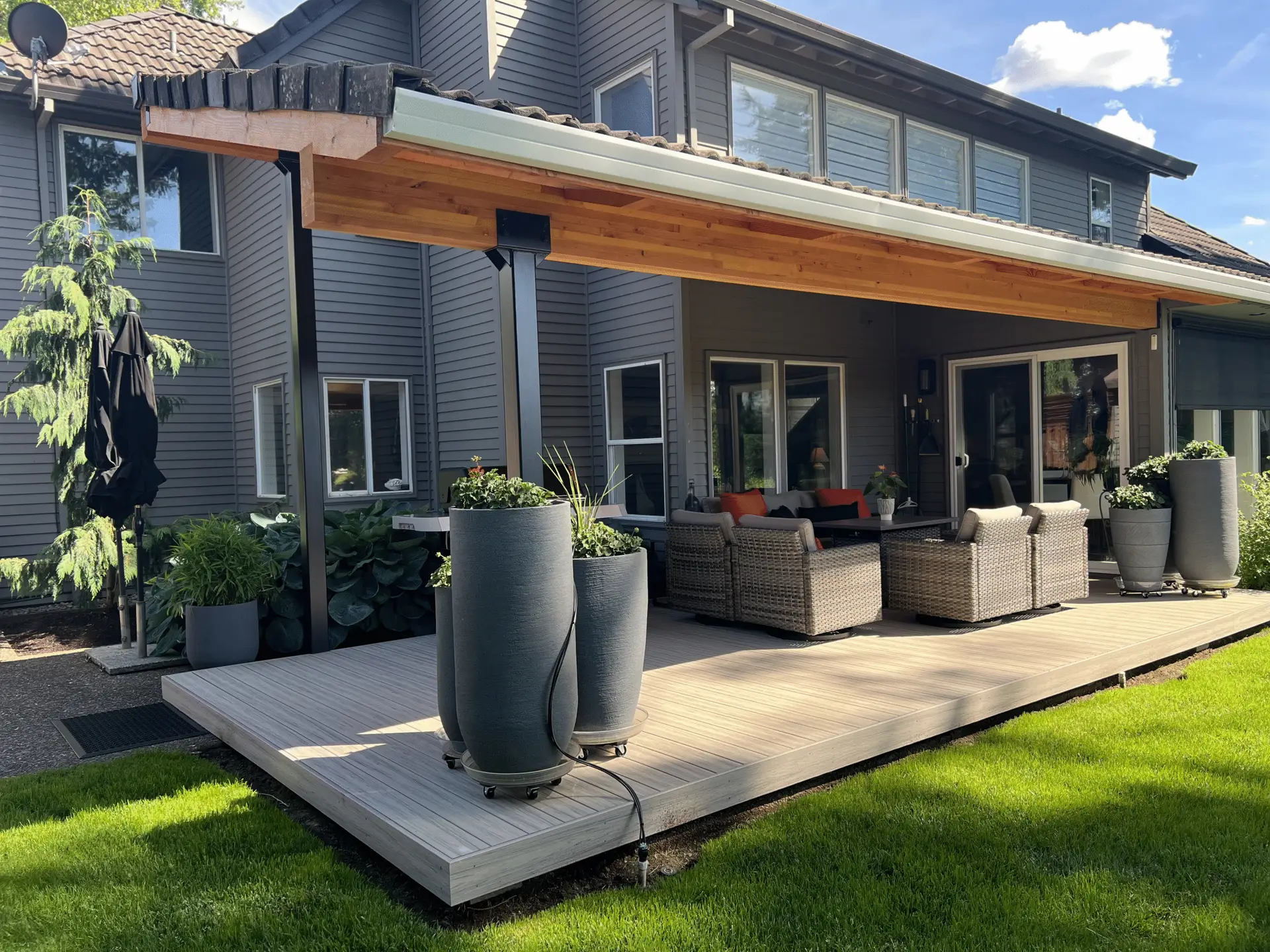Modern custom patio cover with tongue and groove cedar ceiling over composite deck, featuring steel posts and integrated gutter system on a contemporary home
